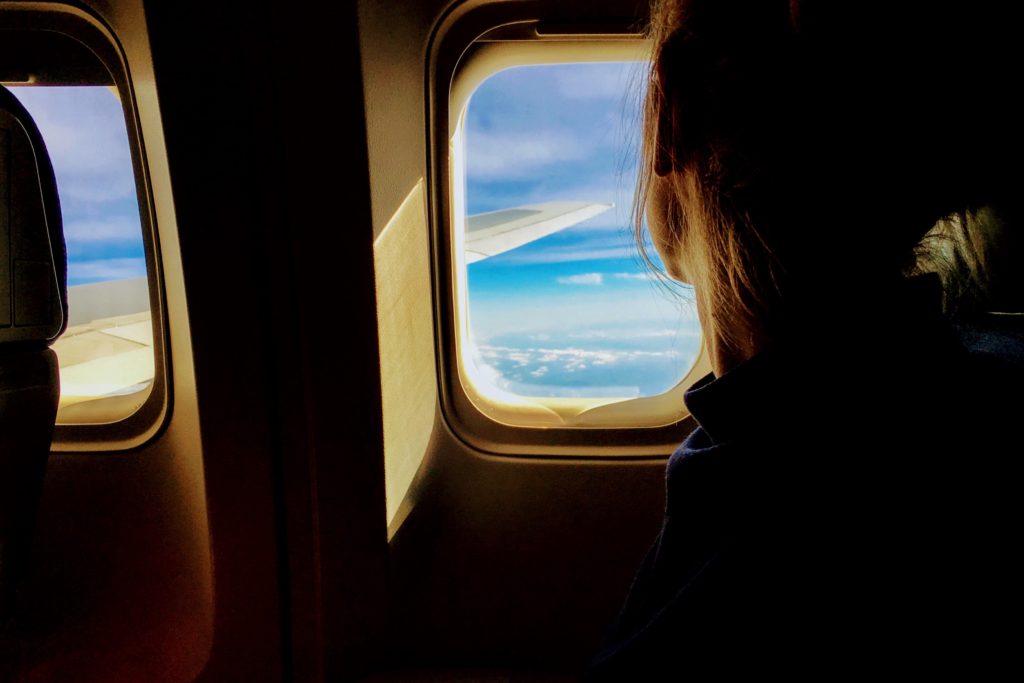 Girl staring out the window on the aisle seat of a plane (probably wondering why she didn't pack these carry on essentials for her flight)