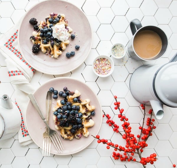 White tile table with breakfast foods like waffles and blueberries and coffee on top