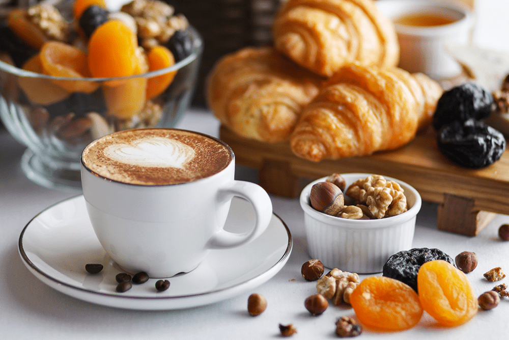 Coffee on a dish with pastries like croissants in background
