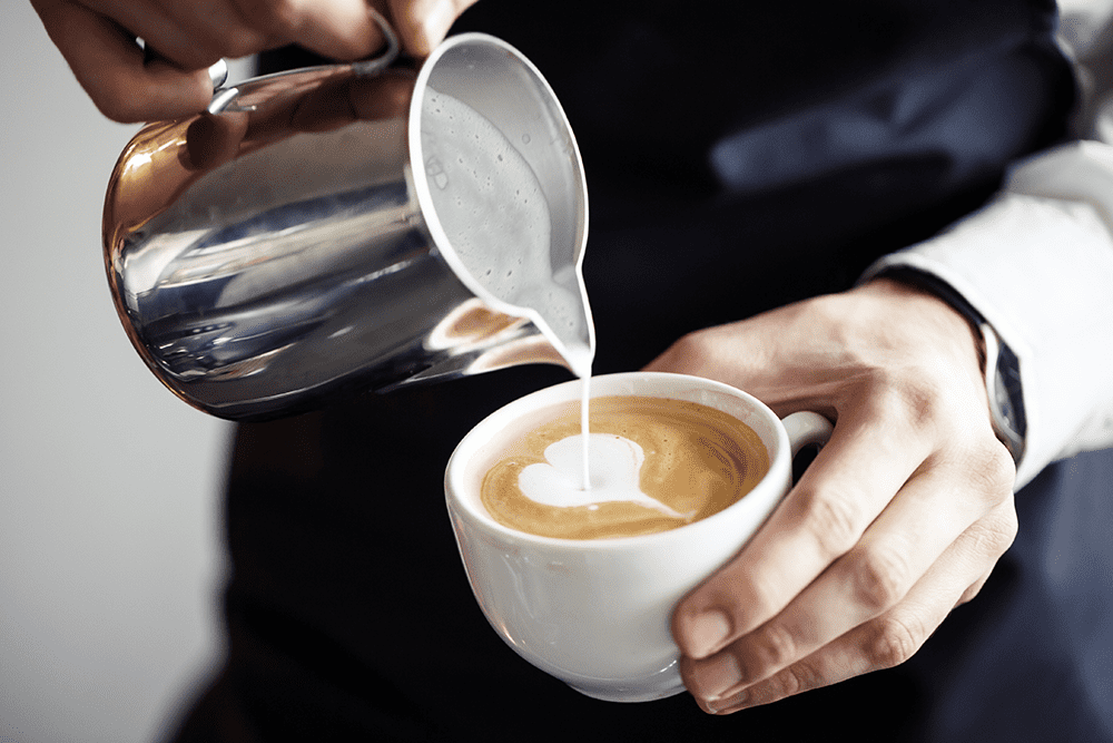 Man pouring milk into a cup forming latte art
