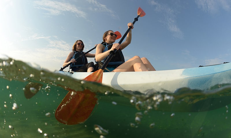 Two young women paddling blue kayak in Atlantic Ocean off of the coast of Florida