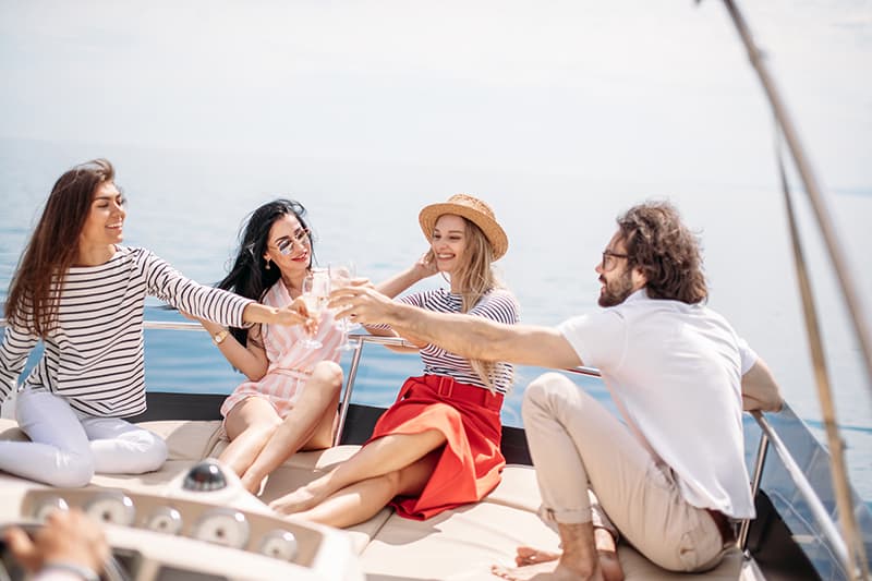 Portrait of young people toasting drinks on a boat and laughing. Cheerful men and woman partying on a boat with amazing seaviews on background.