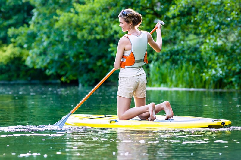 Woman paddle boarding on the water with greenery