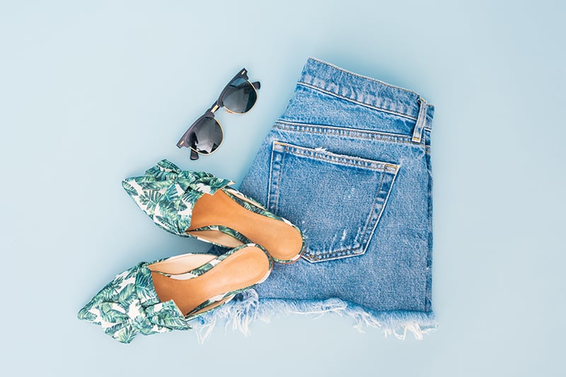 Flat lay of jean shorts and cute flats and sunglasses - examples of what you need to pack for a trip to Miami
