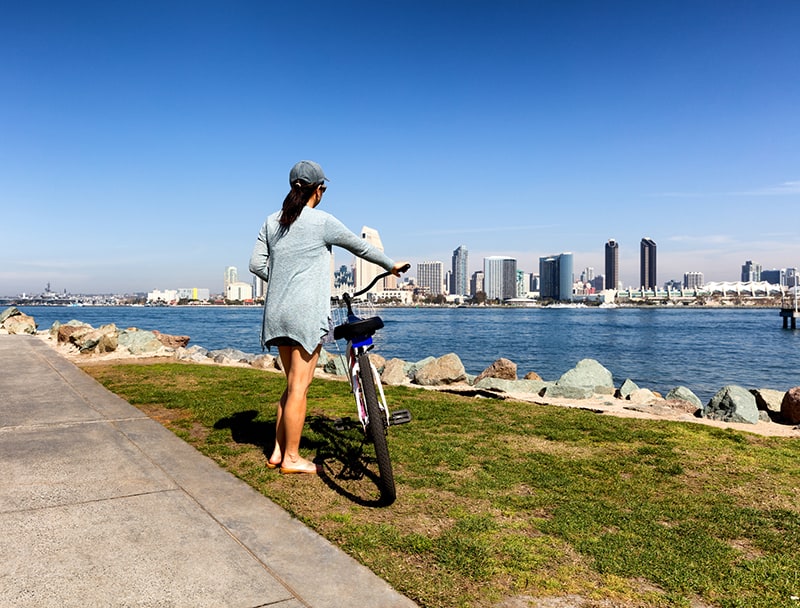 Back view of a woman, holding bicycle, will looking at the bay of San Diego in Southern California.