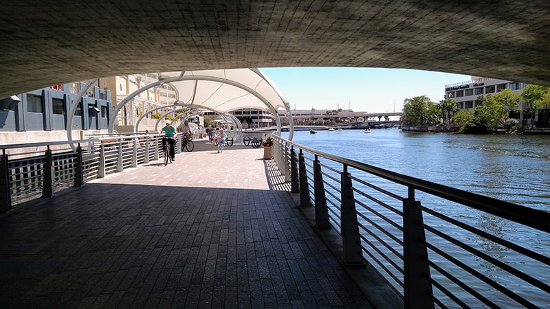 Walking along the Tampa RiverWalk under an overpass with the river nearby