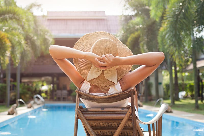 woman in hat taking sunbath near swimming pool - where to stay in each city is a crucial point of vacation planning