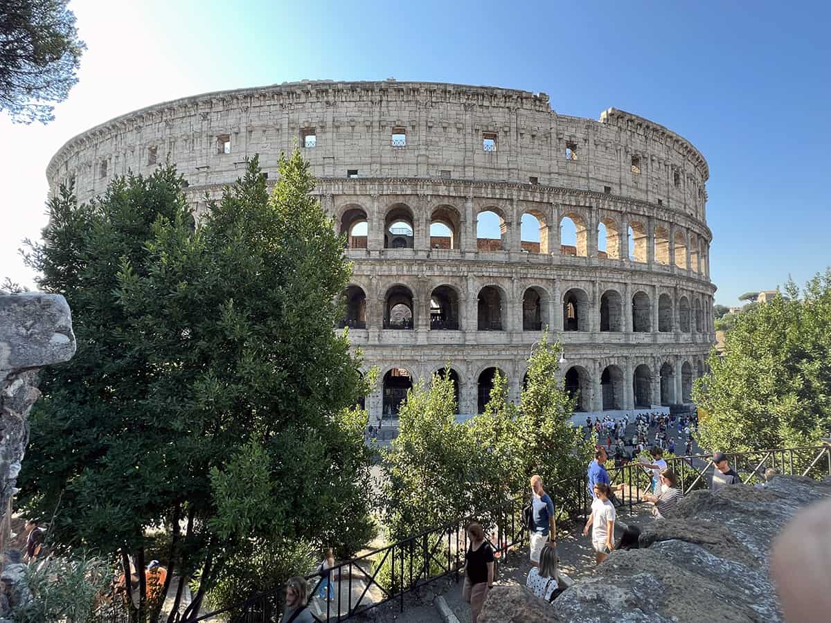 The Colosseum against a blue background with lots of tourists walking in front in Rome Italy