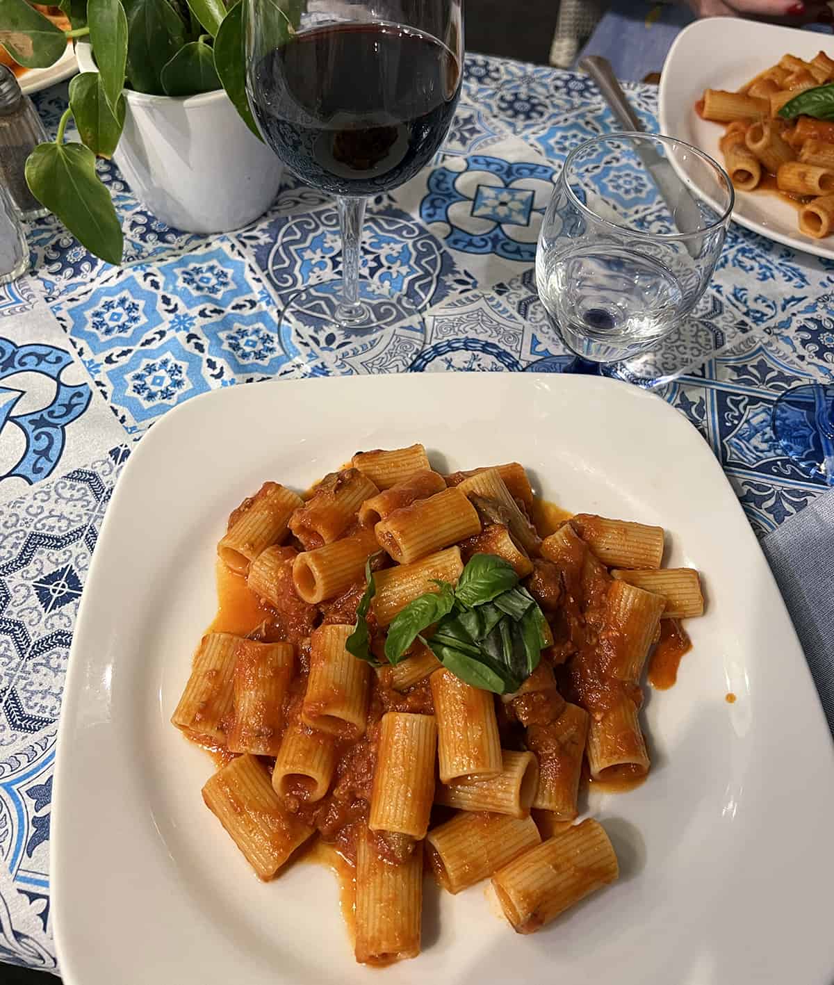 Incredible meat sauce pasta on a blue table cloth with glass of wine