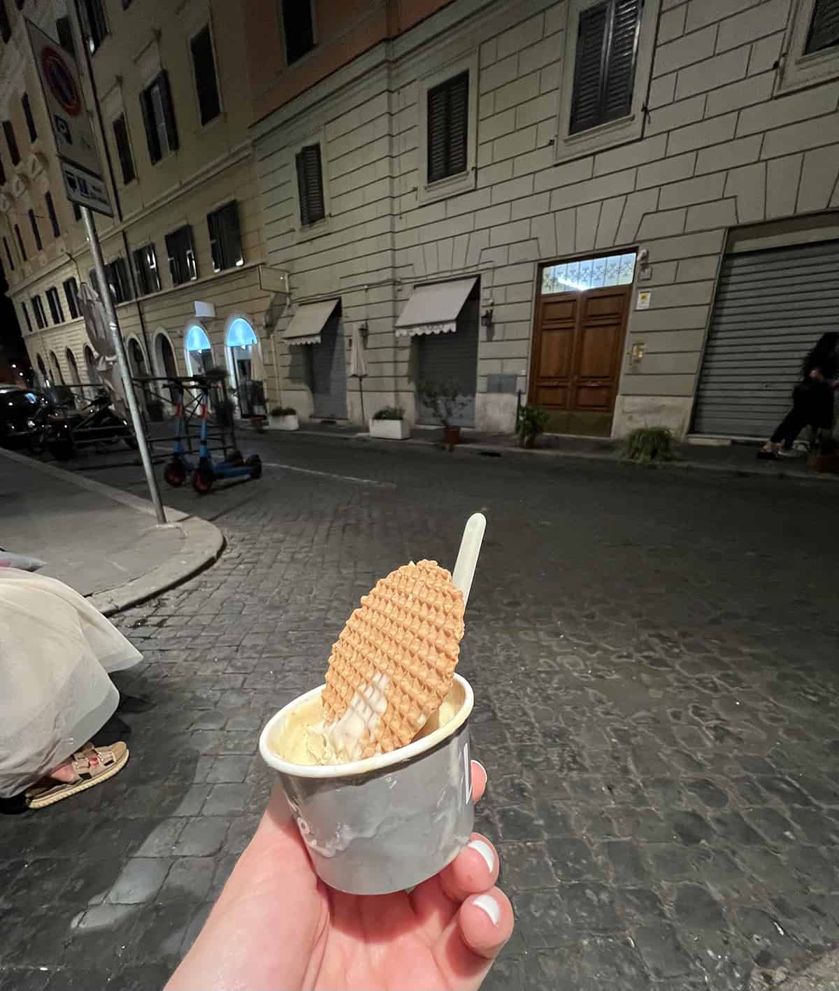 Hand holding up a picture of a cup of gelato with a waffle piece in Rome Italy street